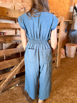 Person wearing a blue denim jumpsuit standing in a rustic wooden barn.