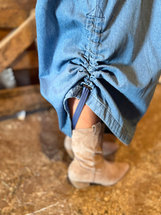 Blue denim skirt and beige cowboy boots on a wooden floor.
