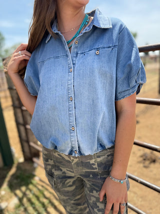 Person wearing a denim shirt and camouflage pants outdoors.