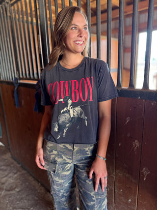 Woman wearing a 'Cowboy' t-shirt in front of horse stalls