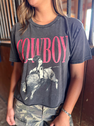 Person wearing a dark gray t-shirt with a graphic of a cowboy on a horse and the word 'COWBOY' in pink.