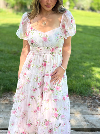 Woman wearing a floral dress standing outdoors on a grassy area.