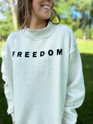Person wearing a light gray sweatshirt with 'FREEDOM' printed on it, standing outdoors.