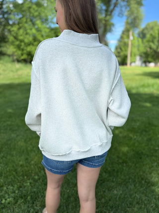 Person wearing a light gray long-sleeve shirt and denim shorts standing on grass with trees in the background