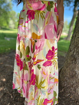 Person wearing a floral dress with pink, yellow, and green colors in an outdoor setting.