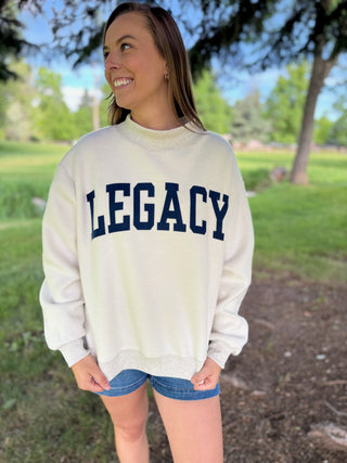 Person wearing a white sweatshirt with 'LEGACY' printed on it, standing outdoors.