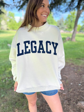 Woman wearing a white sweatshirt with 'LEGACY' printed on it, standing outdoors.