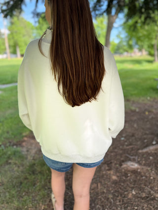 Person wearing a light-colored sweatshirt and denim shorts standing in a park.