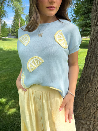 Woman wearing a light blue sweater with lemon designs outdoors