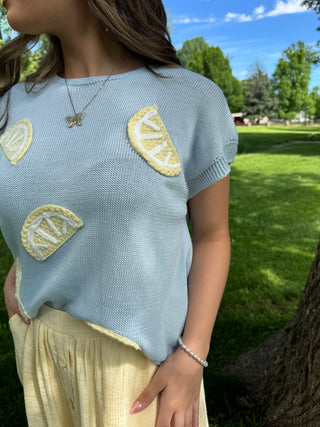 Person wearing a light blue sweater with lemon designs outdoors