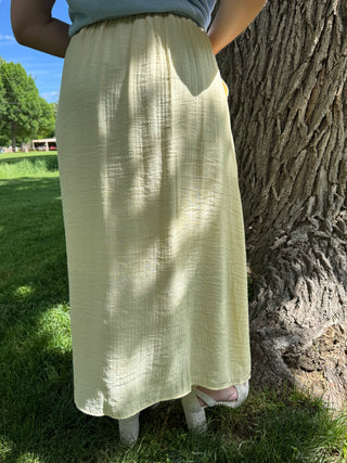 Person wearing a light green skirt standing next to a tree in an outdoor setting