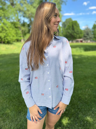 Woman wearing a blue striped shirt with small flags in a park setting