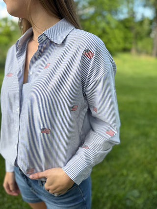 Person wearing a blue and white striped shirt with small American flag patterns outdoors.