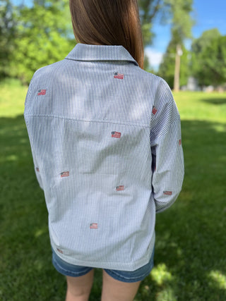 Person wearing a blue and white striped shirt with small flags on the back, standing outdoors.