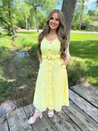 Woman in a yellow dress standing on a wooden bridge in a park.