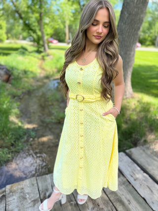 Woman in a yellow dress standing on a wooden deck with greenery in the background