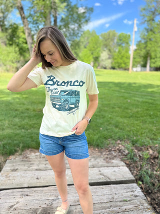 Woman wearing a 'Bronco' t-shirt with a graphic design outdoors on a wooden platform.