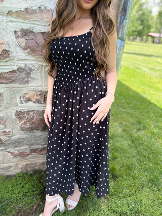 Woman wearing a black polka dot dress standing outdoors against a stone wall.