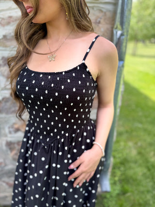Woman wearing a black polka dot dress with a blurred outdoor background