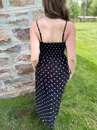 Person wearing a black dress with white polka dots standing in front of a stone wall.
