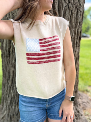Person wearing a sleeveless top with an American flag design, standing next to a tree.