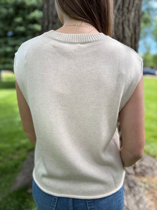 Person wearing a light-colored sleeveless sweater in an outdoor setting