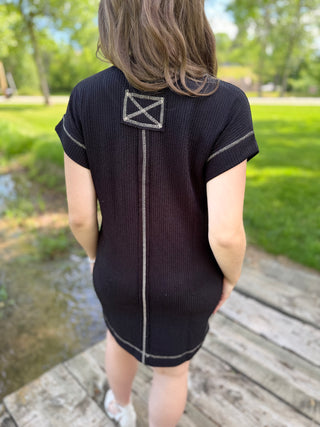 Person wearing a black dress with a white design on the back, standing outdoors.