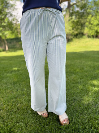 Person wearing light blue striped pants standing on grass with trees in the background
