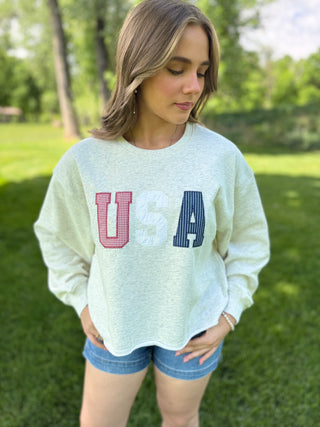 Woman wearing a light green sweatshirt with 'USA' printed on it, standing outdoors.