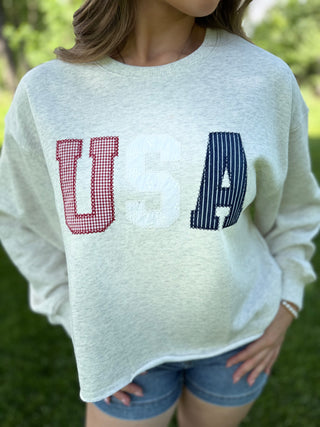 Person wearing a light green sweatshirt with 'USA' printed on it, standing outdoors.