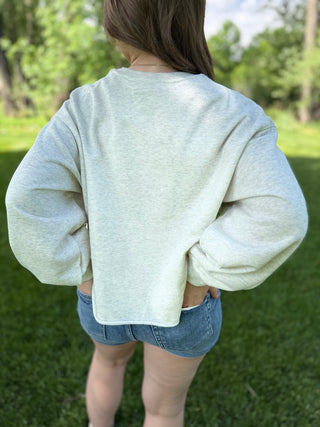 Person wearing a light gray oversized sweater and denim shorts standing in a grassy area with trees.
