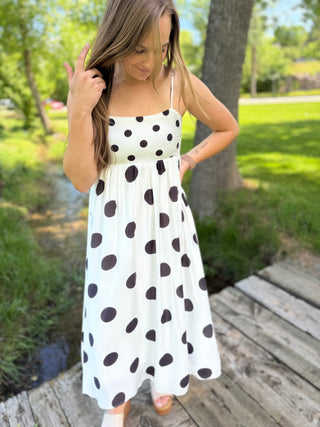 Girl standing outside wearing a black and white polka dot flowy dress.