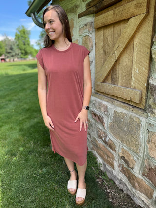 Model standing by barn wearing rust modal dress.
