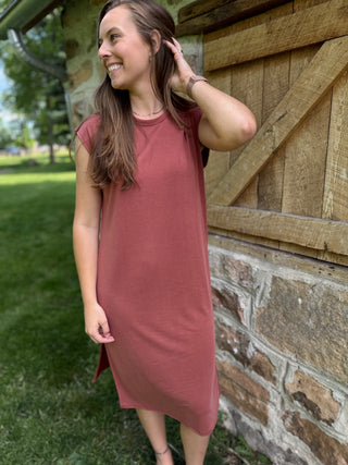 Model standing by barn wearing rust modal dress.