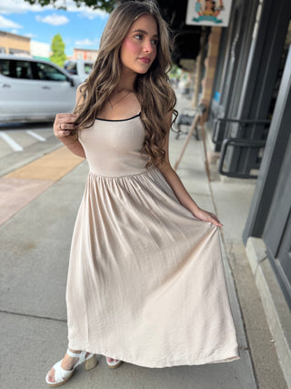 Woman in a beige dress standing on a sidewalk with a city street background