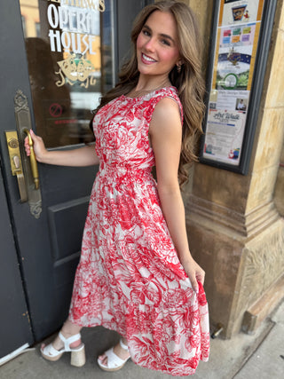 Woman in a red and white floral dress standing outside a building.