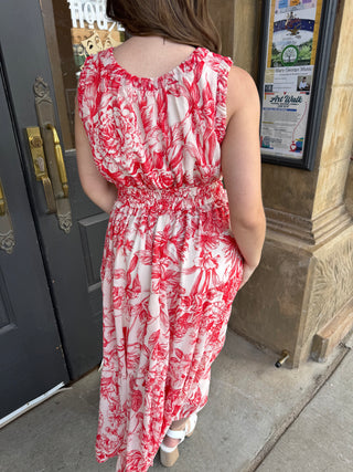 Person wearing a red and white floral dress standing outside a building.