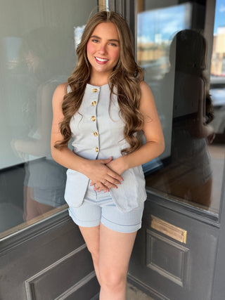 Woman in light blue outfit standing in front of a door with reflections.