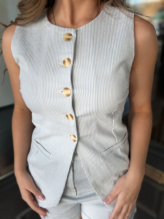 Person wearing a sleeveless striped blazer with gold buttons.