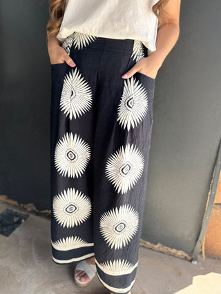 Person wearing black pants with white floral patterns against a gray wall.