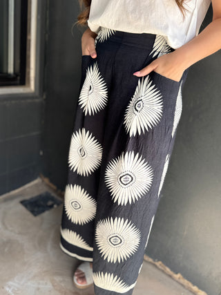Person wearing black pants with white floral patterns against a dark wall.