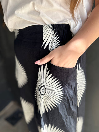 Person wearing a white blouse and black pants with white floral patterns.