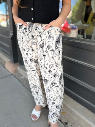 Person wearing black and white floral pants standing on a sidewalk.