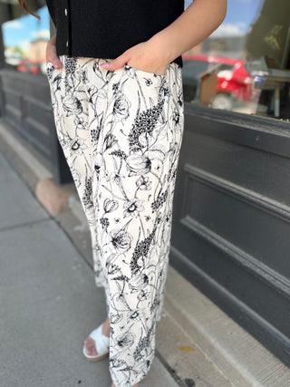 Person wearing black and white floral pants standing on a sidewalk.