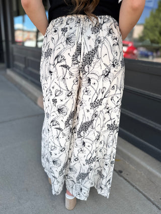Person wearing a black and white floral patterned pants on a sidewalk.