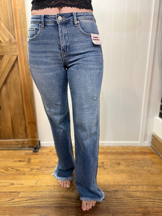 Person wearing blue jeans standing on a wooden floor with a neutral background