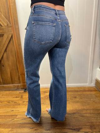 Person wearing blue jeans standing on a wooden floor with a white wall in the background