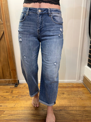 Person wearing blue jeans standing on a wooden floor with a white wall background