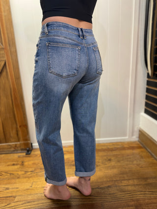 Person wearing blue jeans standing on a wooden floor with a white wall background