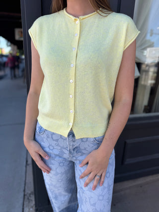 Person wearing a light yellow cardigan over a patterned shirt with blue jeans, standing outdoors.